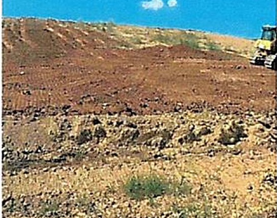 A further view of the bare landfill slope with equipment at the top edge against a blue sky.